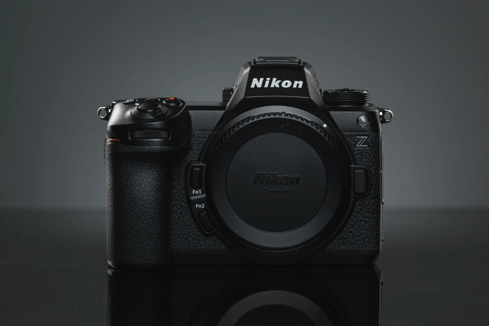 A black Nikon Z6 III mirrorless camera, seen from the front with a cap over its lens mount, stands on a glossy surface against a dark gray background.