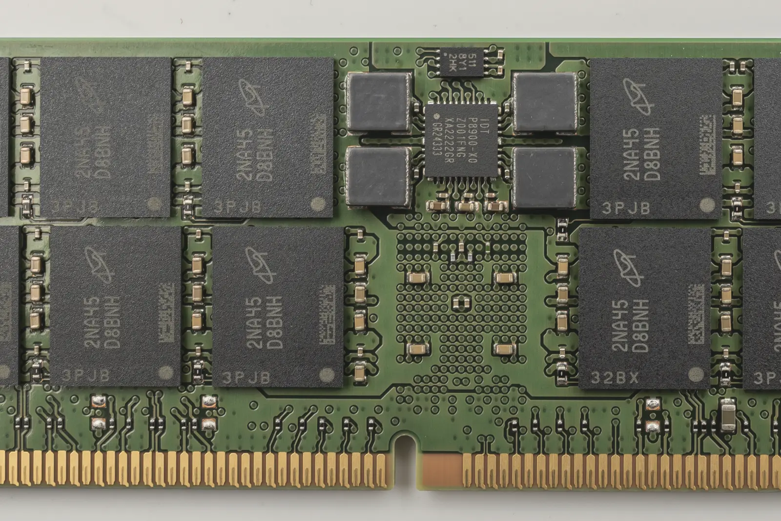 Close-up of the middle of a green memory module: black memory chips in two rows on either side of a small black chip flanked by four gray square components, above a row of gold contacts with a notch.