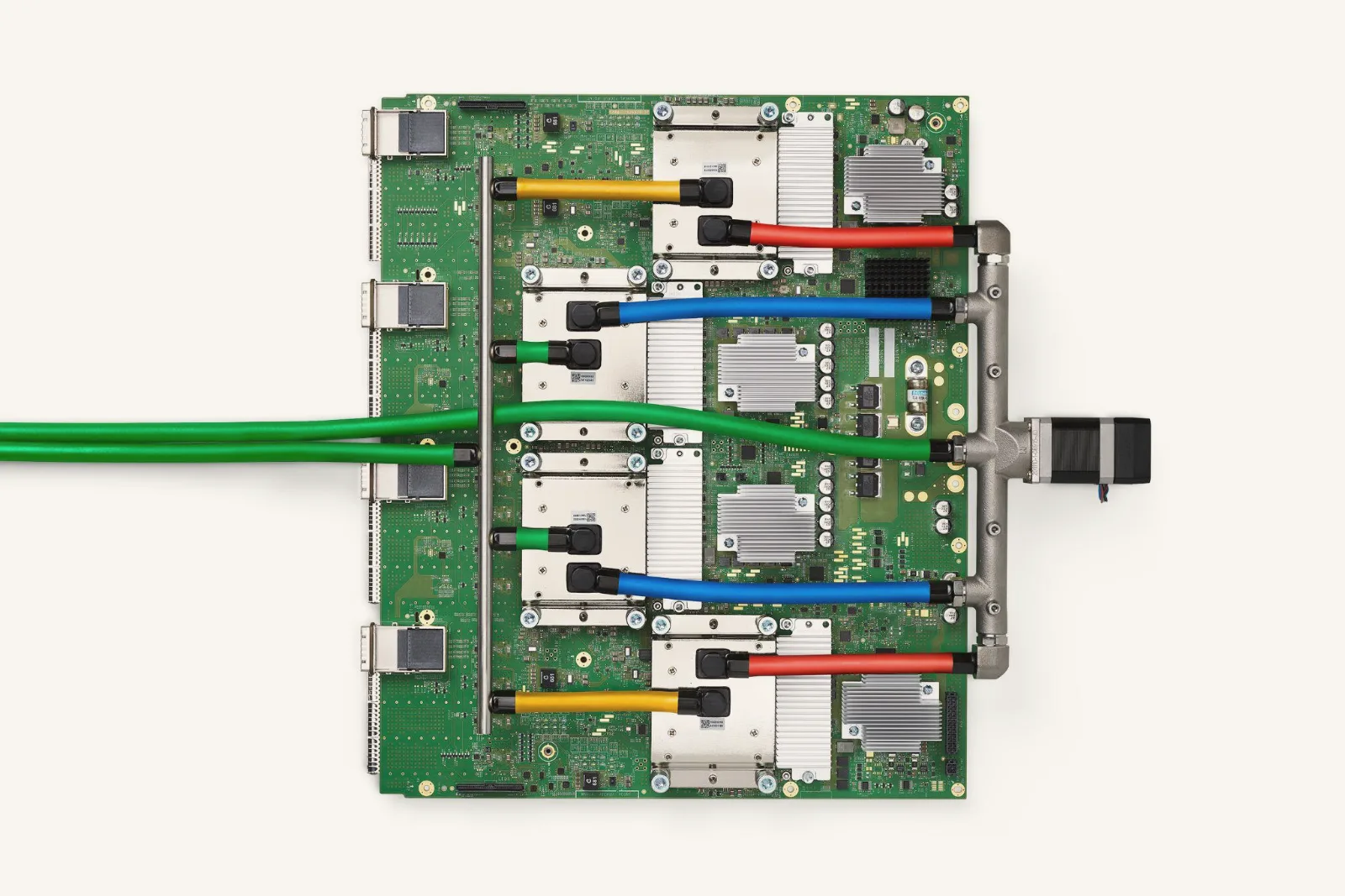 A green circuit board seen from above on a white background, with four chips under metal cooling plates linked by red, blue, yellow and green coolant hoses.