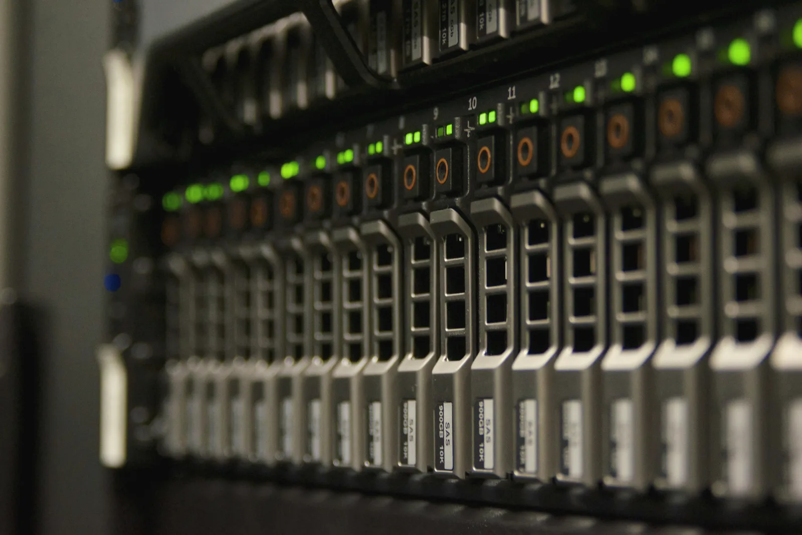 A close-up of a server's front panel: a row of silver drive trays with green status lights, sharp in the middle and blurred toward the edges.